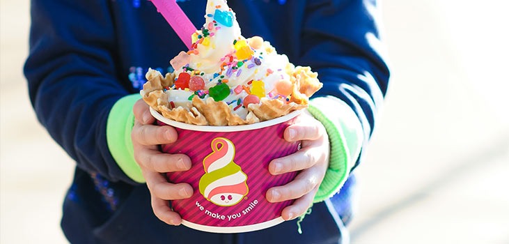 A child holding a Menchie's frozen yogurt cup covered in toppings