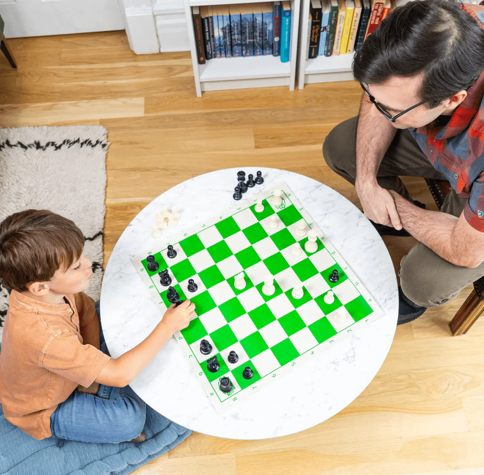 A young child and an adult play together on a chessboard at home.