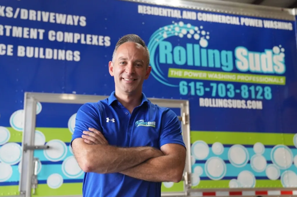 A Rolling Suds team member standing in front of a branded power washing truck.