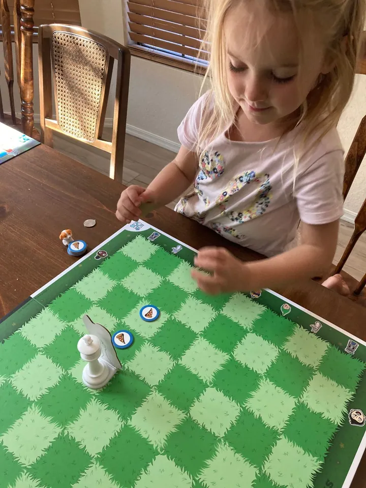 A young blonde girl plays chess on a Story Time Chess green character board.